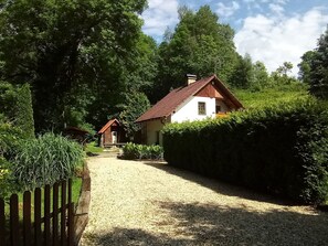 Ein Kiesweg führt zu einem weißen Gebäude mit rotem Dach, umgeben von dichtem Grün und einem Holzzaun.