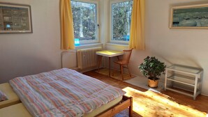 A bedroom with a bed, a desk, a chair, a radiator, and a window with curtains. - Daniela by Interhome (Carlsbad)