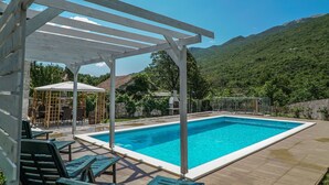 Una piscina con pérgola, sillas de descanso y una zona de estar cubierta.
