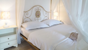 Una cama con dosel, ropa de cama blanca y una mesita de noche con lámpara.