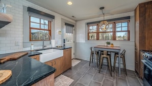 A kitchen with a central island, a dining area with chairs, and a view through large windows. - Little Falls Bungalow (Brevard)