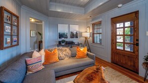 A living room with a grey sofa, wooden door, and framed artwork on the walls. - Little Falls Bungalow (Brevard)