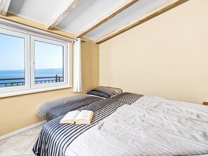 Un dormitorio con cama, ventana y vista al mar.