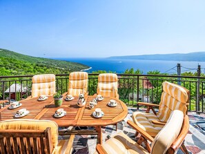 A terrace with a wooden table and striped chairs, overlooking a scenic coastline. - Vacation home Elisa by Interhome (Plomin)
