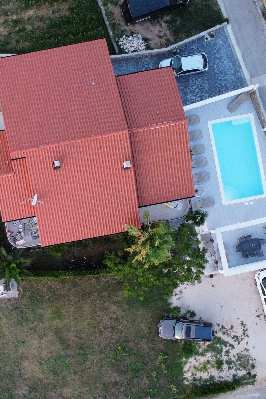 An aerial view of a house with a red roof, a swimming pool, and a patio area with outdoor furniture.