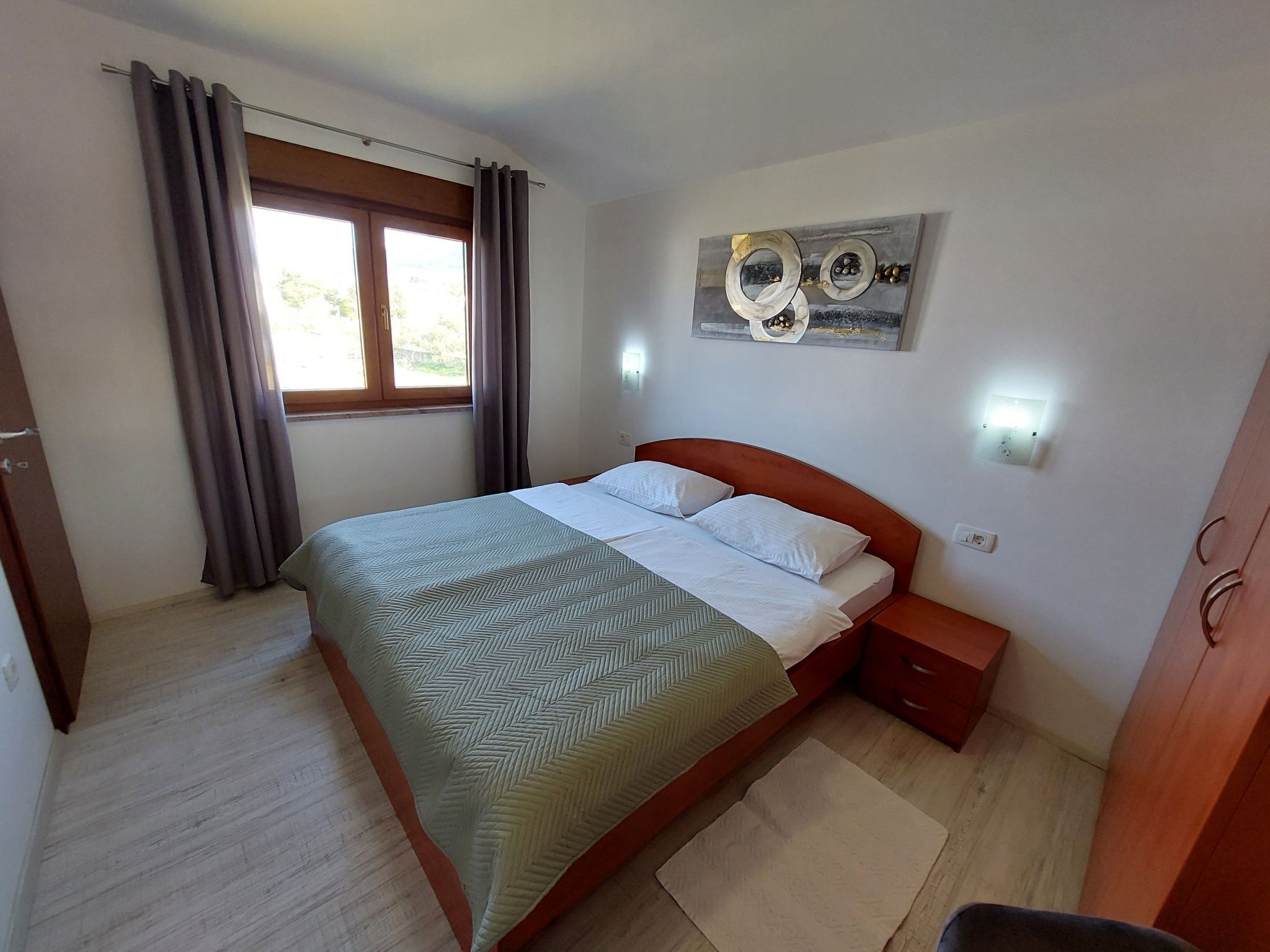 Een slaapkamer met een bed, een nachtkastje, een wandlamp en een raam met gordijnen.