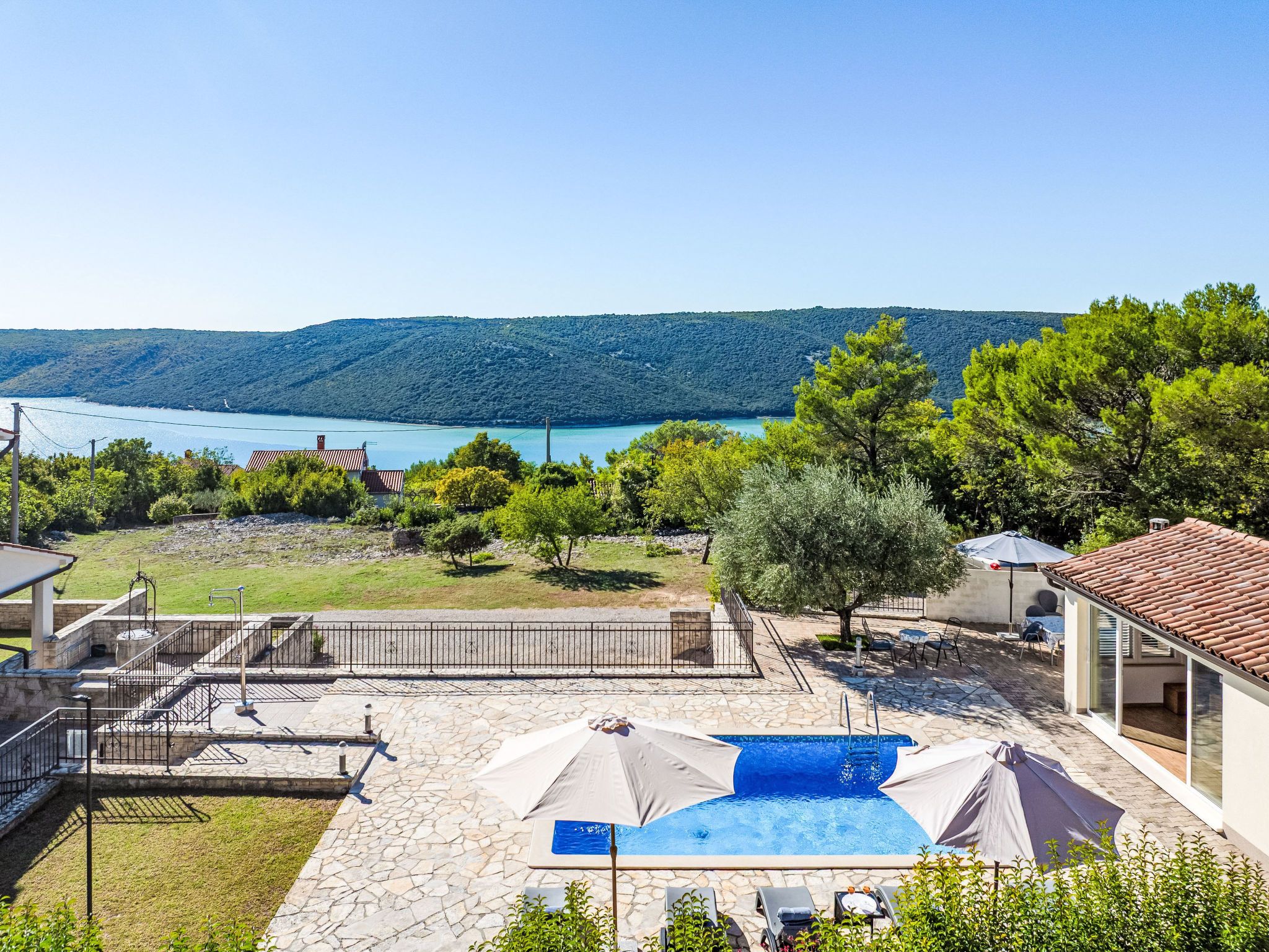 A residential property with a swimming pool, stone patio, and a view of a lake and hills.