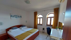 Ein Schlafzimmer mit einem Bett, einem Schreibtisch, zwei Fenstern und einem Bild an der Wand.