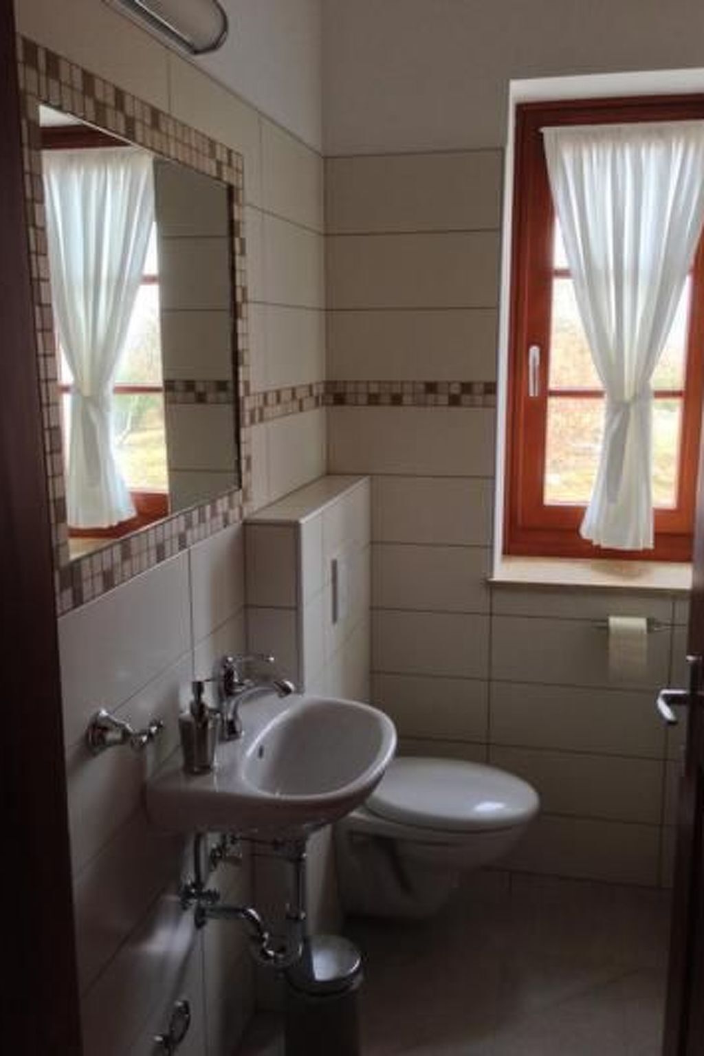 Ein Badezimmer mit Waschbecken, Toilette und einem Fenster mit Vorhängen.