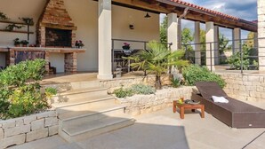 Une terrasse avec un foyer en briques, des sièges d’extérieur et une pergola.