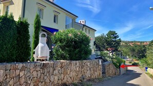 A two-story building with a stone wall in front, a clear blue sky, and a view of the surrounding landscape. - Studio Savic by Interhome (Krk/Šilo)