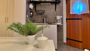 A kitchen with a white countertop, a potted plant, a coffee maker, and a shelf with kitchenware. - Studio Savic by Interhome (Krk/Šilo)