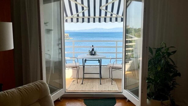 Een kamer met uitzicht op de zee, een glazen deur, een kleine tafel met stoelen en een potplant.