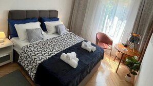 Een hotelkamer met een bed, een plafondventilator, een klein tafeltje met een lamp, een stoel en een raam met gordijnen.