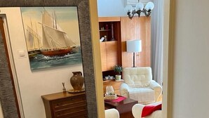 Een kamer met een grote spiegel, een houten dressoir, een witte fauteuil en een rode plaid.
