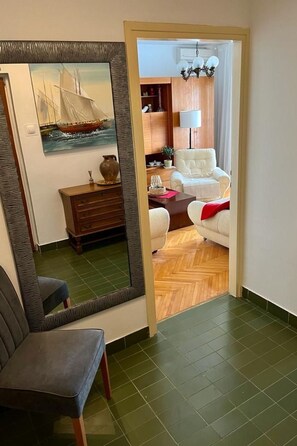 Ein Zimmer mit einem großen Spiegel, einer Holzkommode, einem weißen Sessel und einer roten Decke.