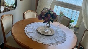 Een ronde houten eettafel met een kantplakje, omringd door vier gestoffeerde stoelen. In het midden staat een vaas met bloemen.