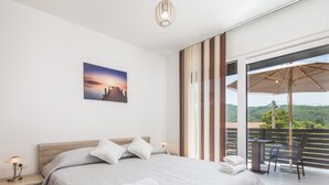 A bedroom with a large bed, a nightstand, a bedside lamp, a view of the outdoors through a sliding door, and a balcony with a table and chairs. - Schönes Haus für 8 Personen mit großem Schwimmbad by Interhome (Drazice)