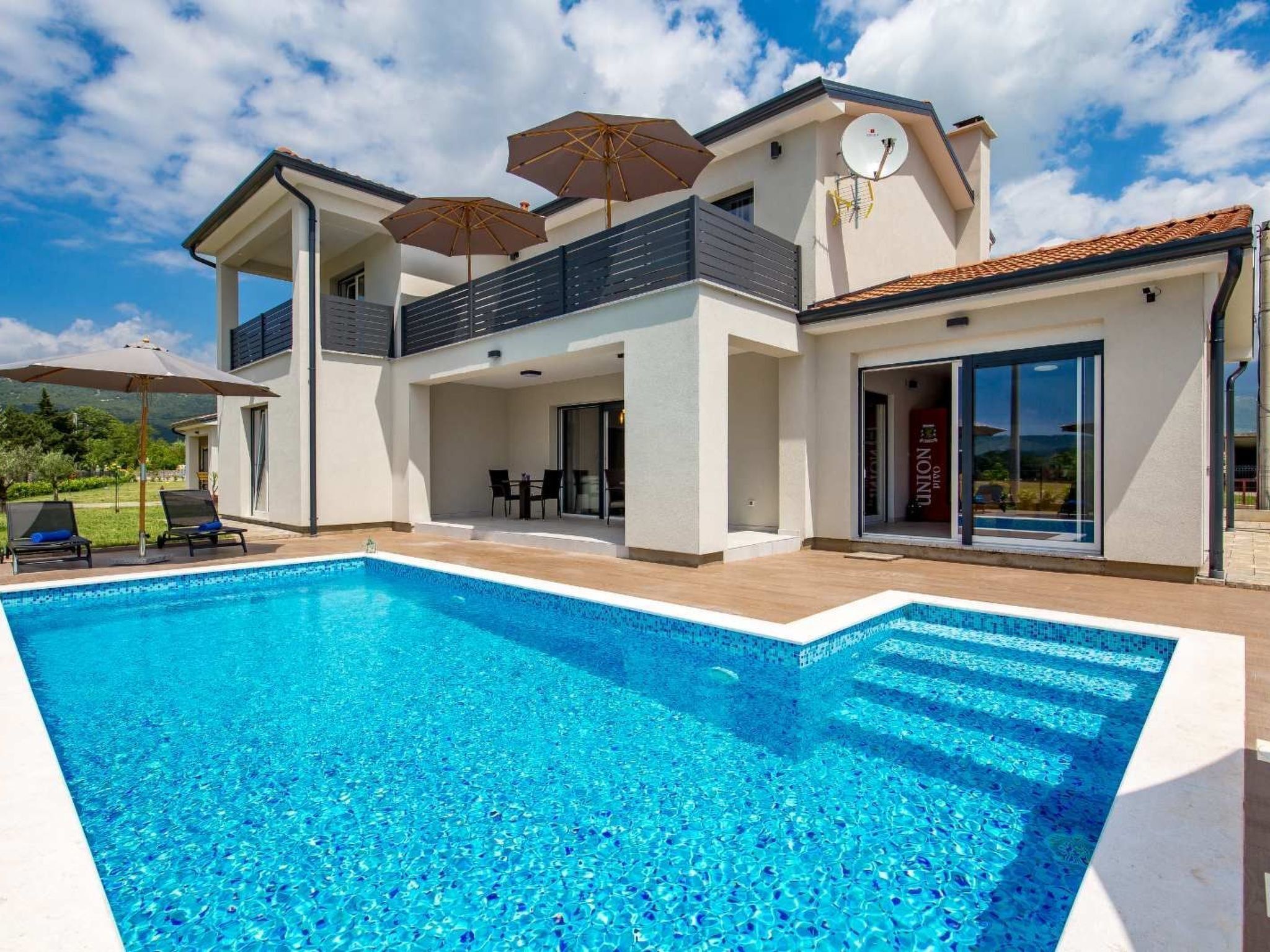 A modern two-story house with a swimming pool, outdoor seating, and a large window.