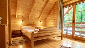 A wooden cabin bedroom with a bed, bedside tables, and a view of the outdoors through a large window. - IDEAL FÜR FAMILIEN, PAARE UND NATURLIEBHABER by Interhome (Lokve)