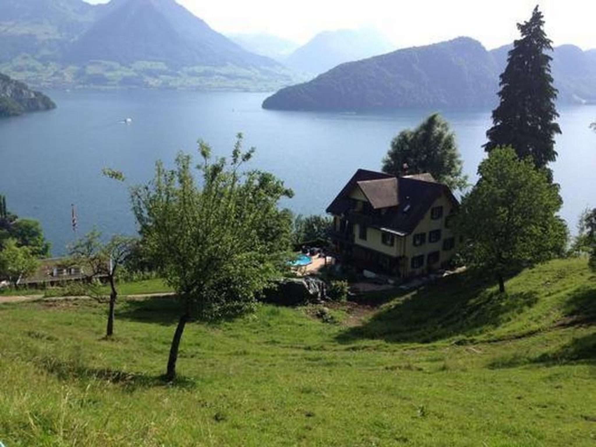 Ett hus med ett sluttande tak, omgivet av en gräsyta och en sjö, med berg i bakgrunden.