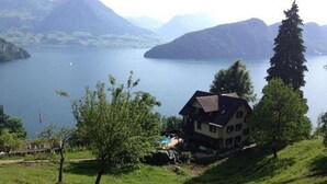 Een huis met schuin dak, omgeven door een gazon en een meer, met bergen op de achtergrond.