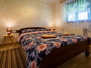 A bedroom with a wooden bed, floral bedding, bedside lamps, a small table, and a window with sheer curtains. - Haus in Sleme Skradsko mit Whirlpool und Parkplatz by Interhome (Sleme Skradsko)