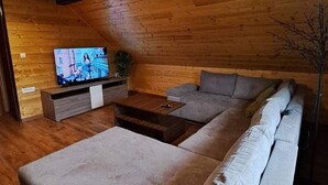 Ett mysigt vardagsrum med en stor hörnsoffa, ett soffbord och en platt-TV som är monterad på en väggpanel i trä.