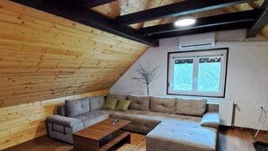 Ett rum i loftstil med ett träpanelat tak, en hörnsoffa, ett soffbord och ett fönster med persienner.