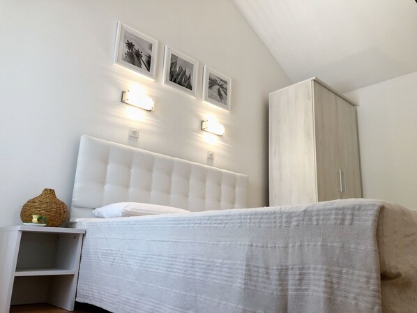 Une chambre à coucher avec un lit blanc, une table de chevet, une armoire et trois appliques murales.