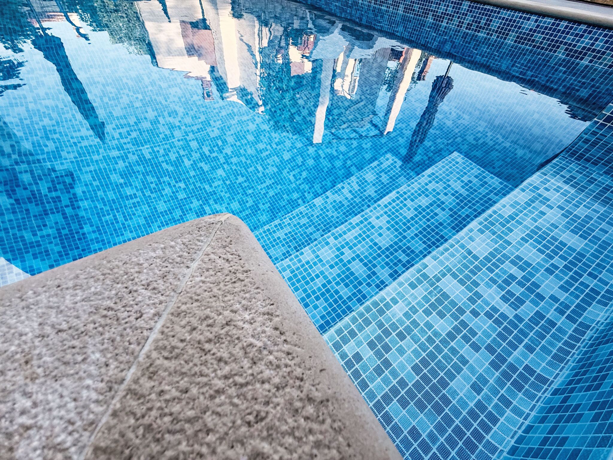 Una piscina azul cristalina con borde de azulejos y un borde de piedra.