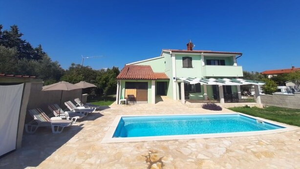 Ein zweistöckiges Haus mit Schwimmbad, Außenbereich mit Sitzgelegenheiten und einer überdachten Terrasse.