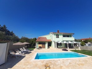 Ein zweistöckiges Haus mit Schwimmbad, Außenbereich mit Sitzgelegenheiten und einer überdachten Terrasse.