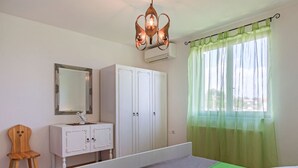 Ein Schlafzimmer mit Bett, Kommode, Stuhl und Fenster mit grünen Vorhängen.