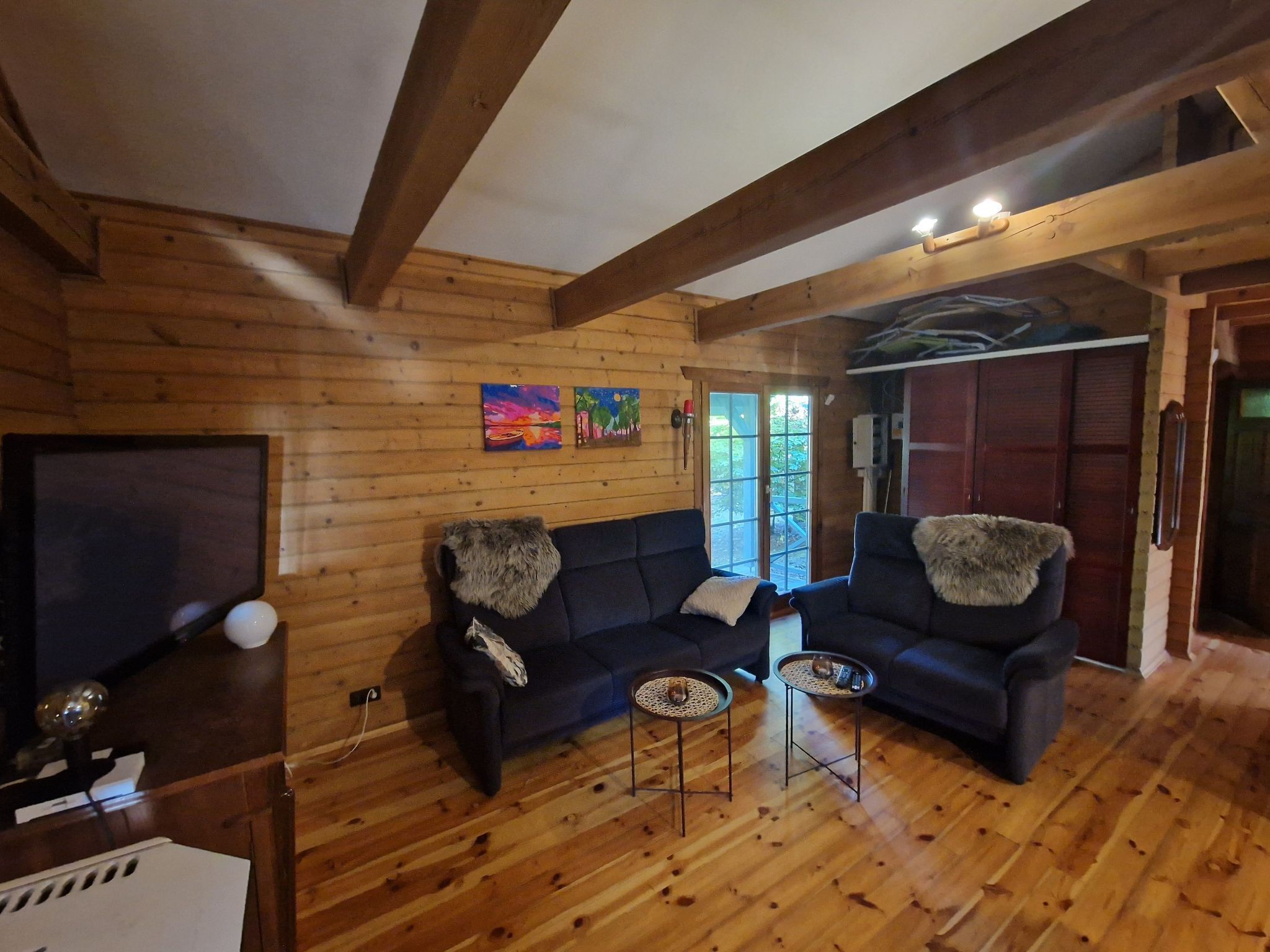 L’intérieur d’un chalet en bois chaleureux et accueillant, avec un canapé, deux petites tables d’appoint et un téléviseur.