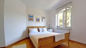 A bedroom with a wooden bed, white bedding, a window with a view of trees, and three framed pictures on the wall. - Wohnung Lungomare, 300m vom Strand entfernt, Pula by Interhome (Pula)