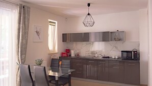 Et moderne køkken med grå skabe, et glasbord og en hængende lampe.
