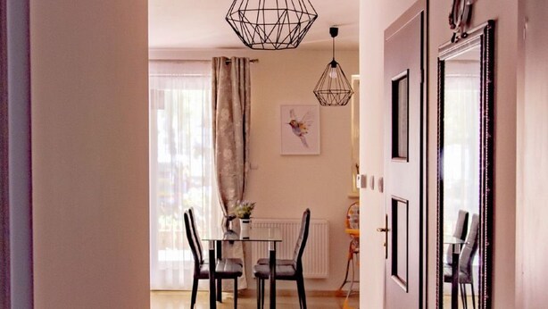 En gang der fører til et spiseområde med et bord og stole, en hængende lampe og et spejl på væggen.