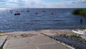 Una platja amb barques i kayak a l'aigua, sorra i un passeig de formigó que mena a la platja.