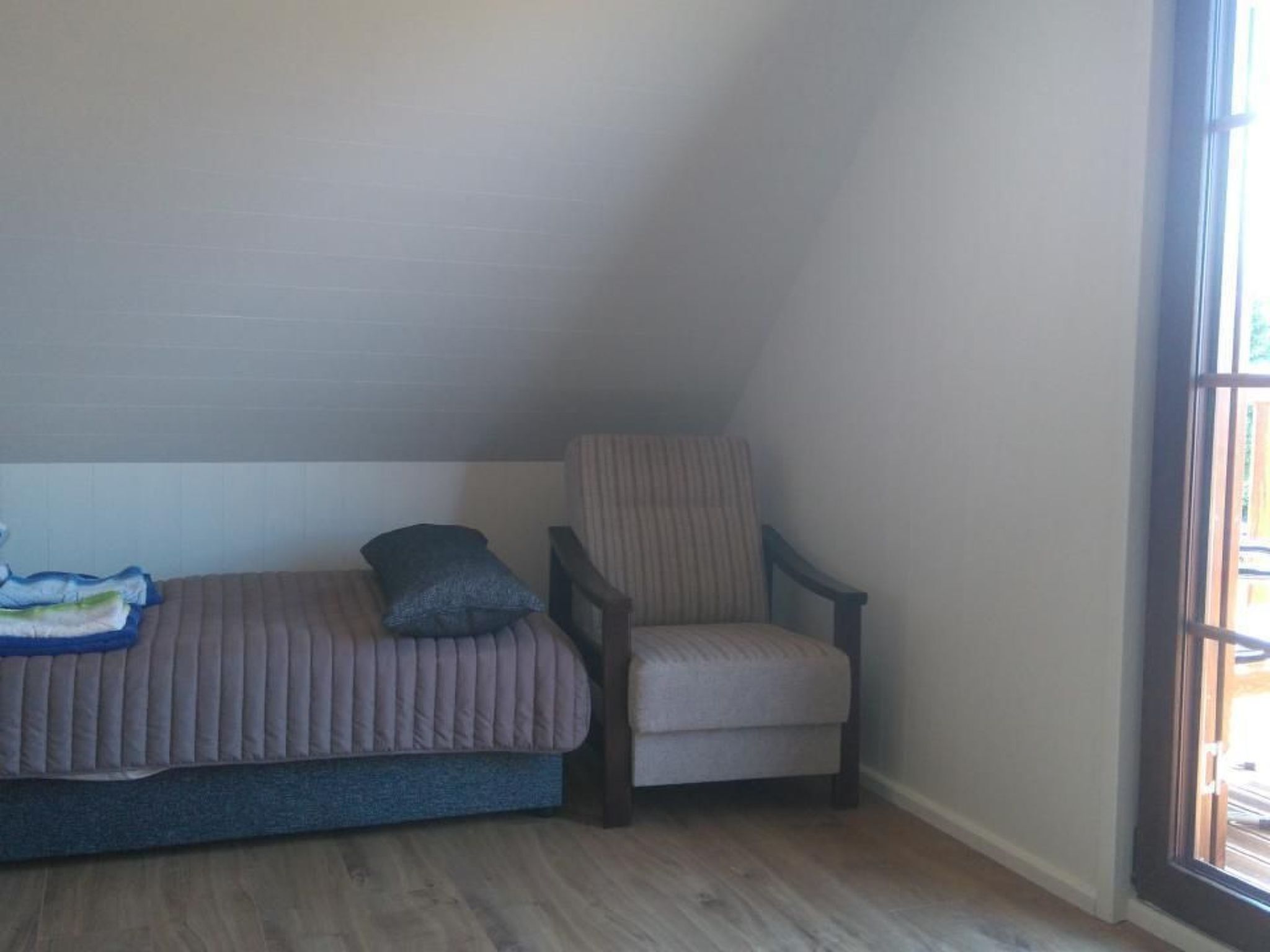 A small, cozy room with a bed, a chair, and a window.