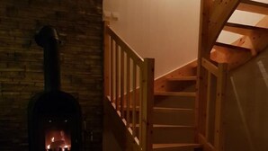 Una habitació acollidora amb una estufa de llenya, una espelma sobre un tapet i una escala.