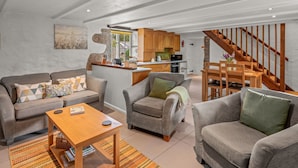 A spacious living area with a sofa set, a coffee table, and a dining table. A kitchen is visible in the background with wooden cabinets and a stone wall. - Idyllisches Landhaus mit wunderschönem Garten by Interhome (Draynes)