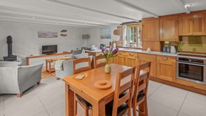 A spacious living area with a fireplace, a dining table with chairs, and a kitchen with wooden cabinets and a stove. - Idyllisches Landhaus mit wunderschönem Garten by Interhome (Draynes)