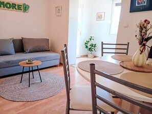 Ett vardagsrum med en soffa, ett matbord med stolar, ett litet bord med en skål och en krukväxt.