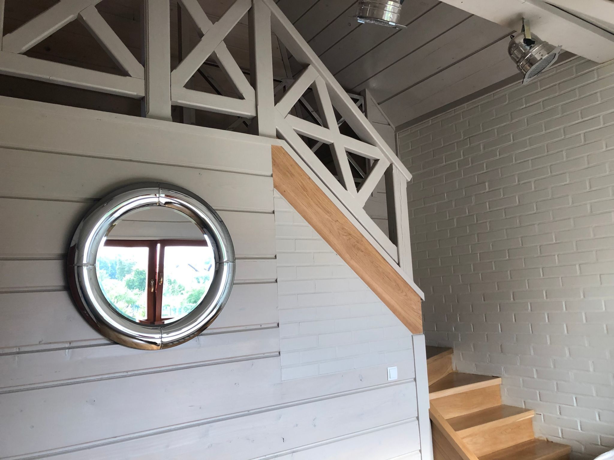 Un escalier avec des rampes blanches et une main courante en bois, menant à un palier doté d’une fenêtre circulaire.
