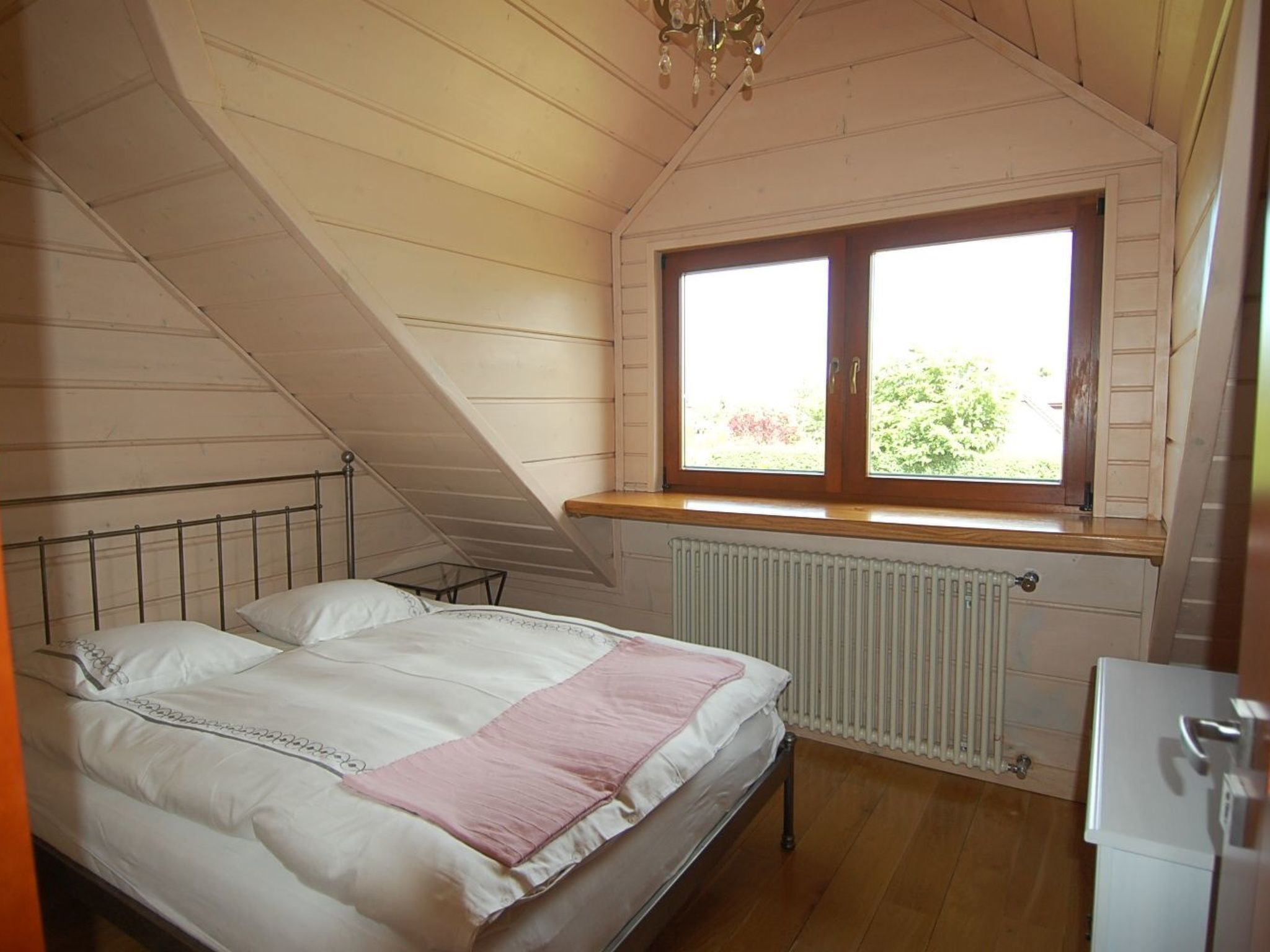 Un dormitorio con cama, ventana, radiador y techo de madera.