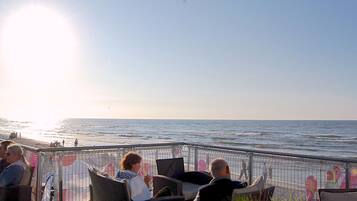Une terrasse avec des chaises en osier donnant sur la mer, une rambarde en métal et un ciel dégagé.