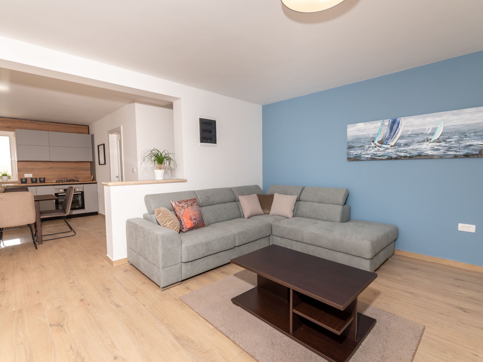 A modern living room with a grey sectional sofa, a wooden coffee table, and a painting of sailboats on the wall.
