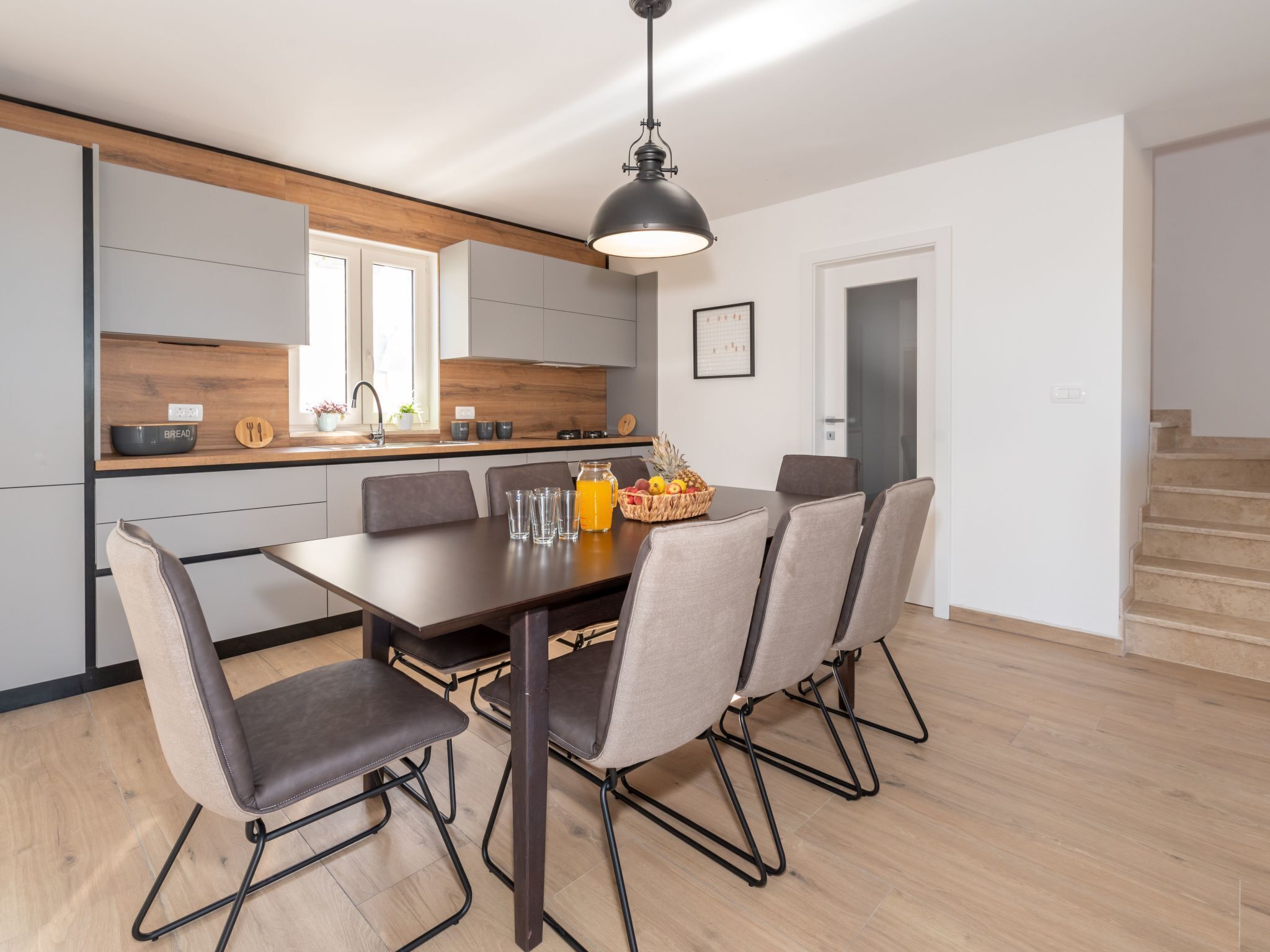 A modern kitchen with a dining area, featuring a wooden countertop, a black pendant light, and a dining table with chairs.