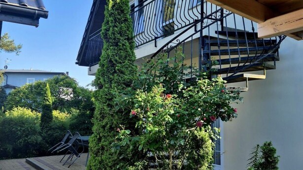 A covered outdoor area with a brick pathway, a wooden pergola, and a staircase leading to a balcony with a black railing. - mit Wasserblick by Interhome (Wisełka)